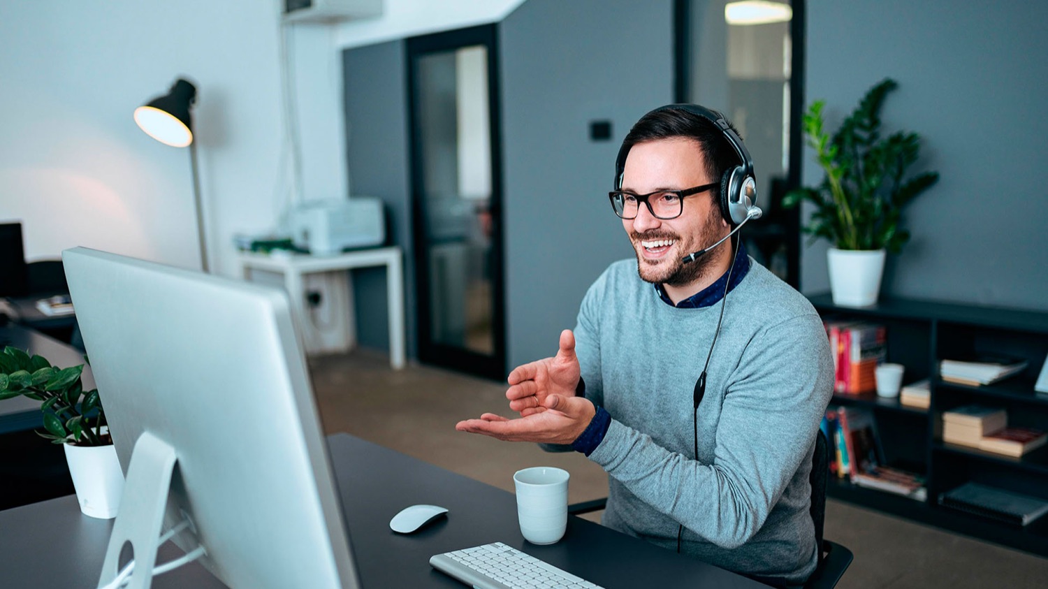 A smiling team member wearing a headset on a call at his desk