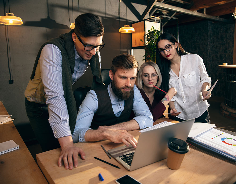 Four colleagues gathered around a laptop in a warm, modern workspace